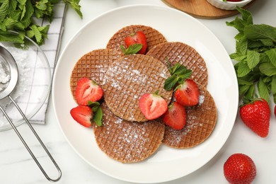 Photo of Tasty Dutch waffles (stroopwafels), mint and strawberries on white marble table, flat lay
