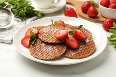 Photo of Tasty Dutch waffles (stroopwafels), mint and strawberries on white marble table, closeup
