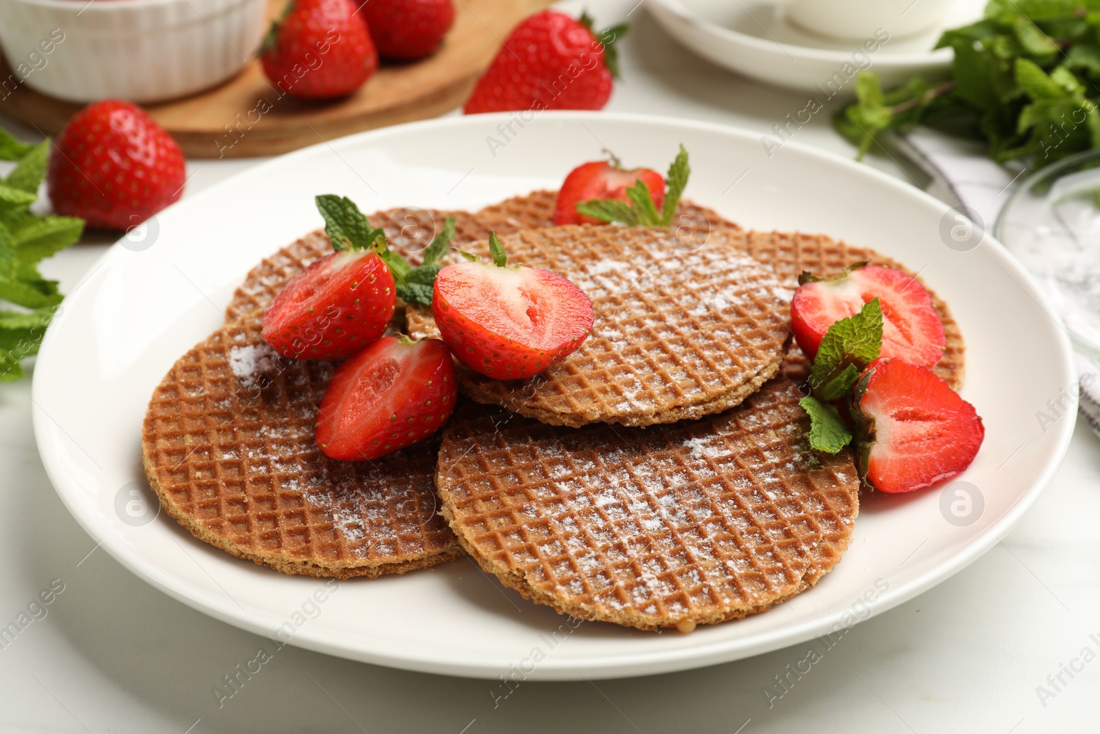 Tasty Dutch waffles (stroopwafels), mint and strawberries on white marble table, closeup Photo of Tasty Dutch waffles (stroopwafels), mint and strawberries on white marble table, closeup