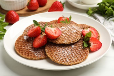 Photo of Tasty Dutch waffles (stroopwafels), mint and strawberries on white marble table, closeup