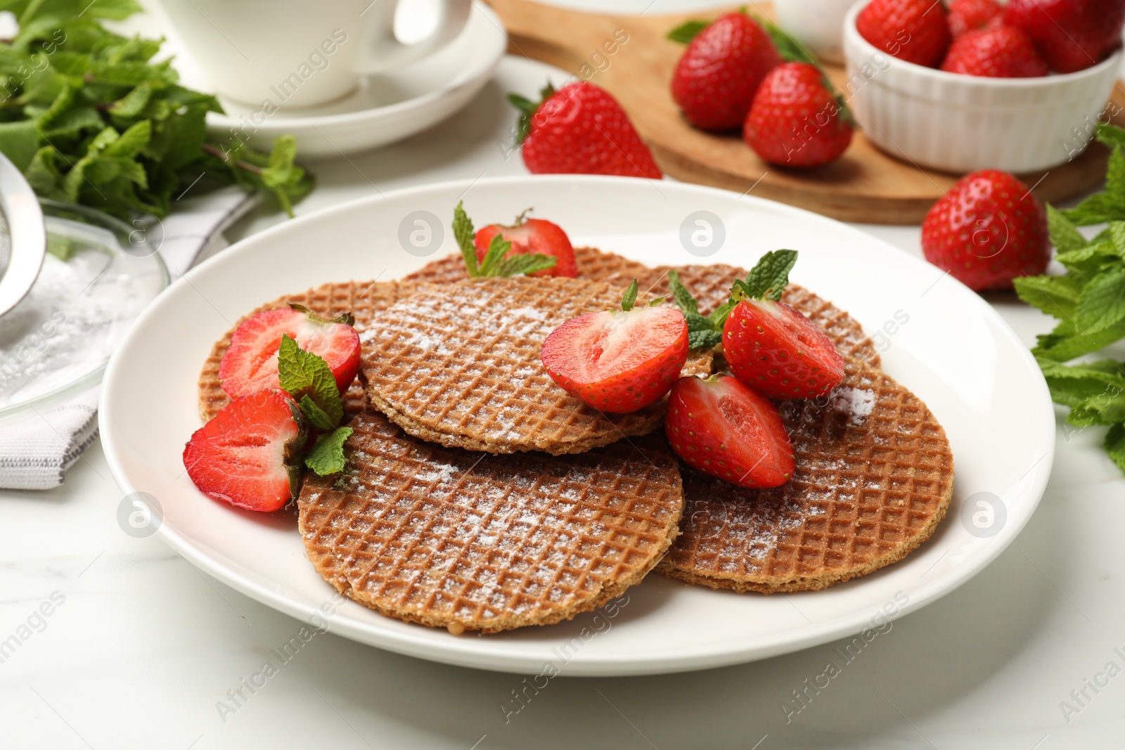 Tasty Dutch waffles (stroopwafels), mint and strawberries on white marble table, closeup Photo of Tasty Dutch waffles (stroopwafels), mint and strawberries on white marble table, closeup