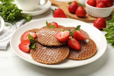 Photo of Tasty Dutch waffles (stroopwafels), mint and strawberries on white marble table, closeup