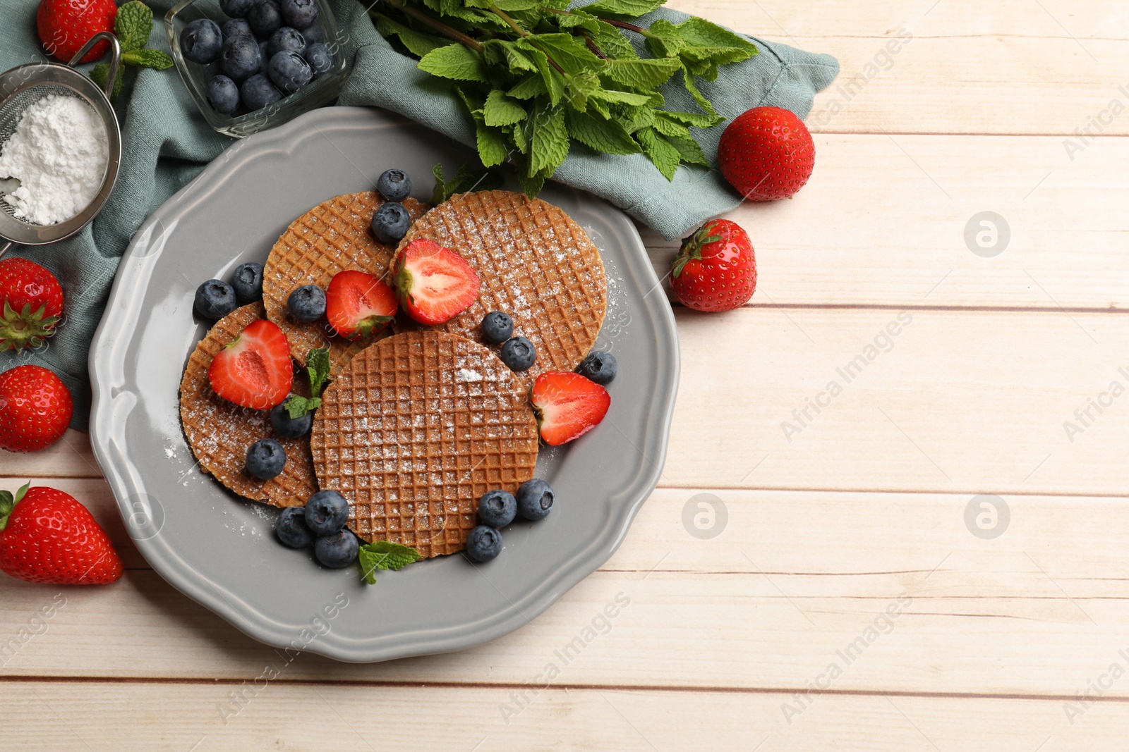 Tasty Dutch waffles (stroopwafels), mint and berries on light wooden table, flat lay. Space for text Photo of Tasty Dutch waffles (stroopwafels), mint and berries on light wooden table, flat lay. Space for text