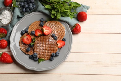 Photo of Tasty Dutch waffles (stroopwafels), mint and berries on light wooden table, flat lay. Space for text