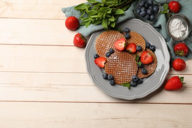 Photo of Tasty Dutch waffles (stroopwafels), mint and berries on light wooden table, flat lay. Space for text