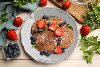 Photo of Tasty Dutch waffles (stroopwafels), mint and berries on light wooden table, flat lay