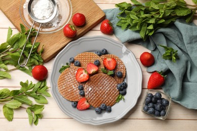 Photo of Tasty Dutch waffles (stroopwafels), mint and berries on light wooden table, flat lay