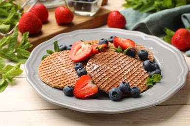 Photo of Tasty Dutch waffles (stroopwafels), mint and berries on light wooden table, closeup