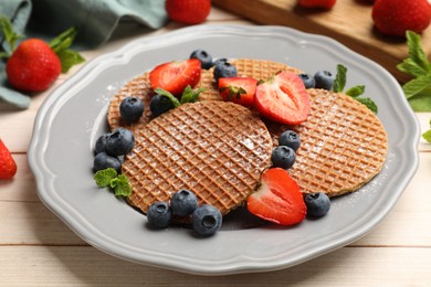 Photo of Tasty Dutch waffles (stroopwafels), mint and berries on light wooden table, closeup