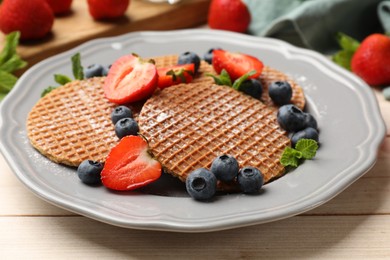 Photo of Tasty Dutch waffles (stroopwafels), mint and berries on light wooden table, closeup