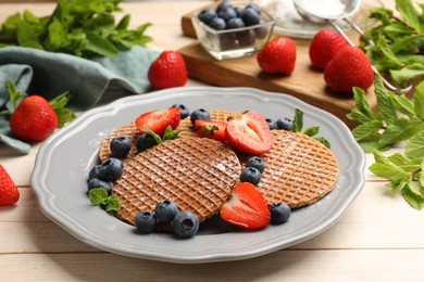 Photo of Tasty Dutch waffles (stroopwafels), mint and berries on light wooden table, closeup