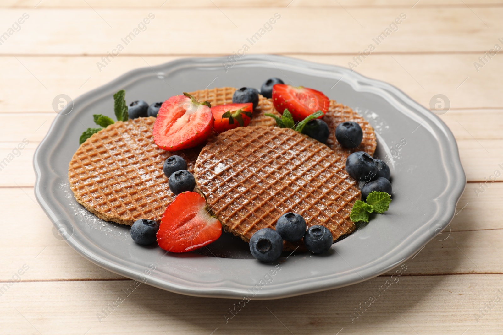 Tasty Dutch waffles (stroopwafels), mint and berries on light wooden table, closeup Photo of Tasty Dutch waffles (stroopwafels), mint and berries on light wooden table, closeup