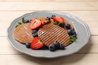 Photo of Tasty Dutch waffles (stroopwafels), mint and berries on light wooden table, closeup