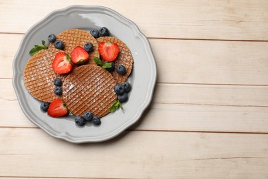 Photo of Tasty Dutch waffles (stroopwafels), mint and berries on light wooden table, top view. Space for text