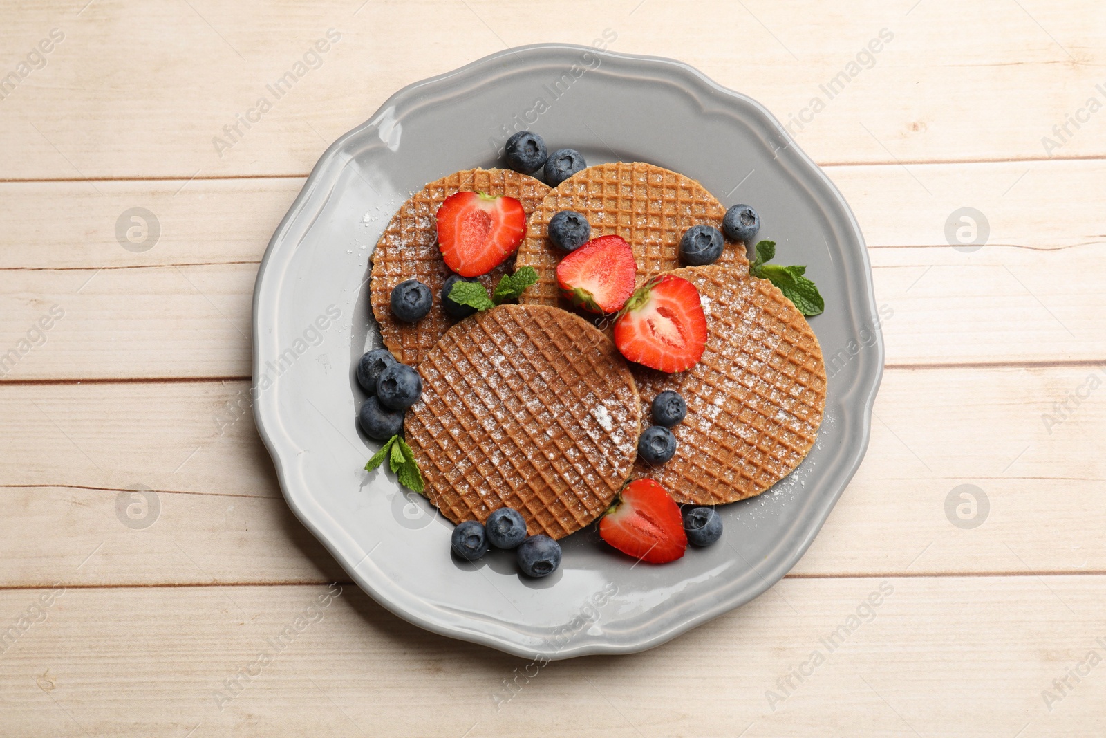 Tasty Dutch waffles (stroopwafels), mint and berries on light wooden table, top view Photo of Tasty Dutch waffles (stroopwafels), mint and berries on light wooden table, top view