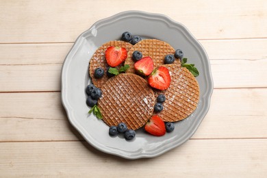 Photo of Tasty Dutch waffles (stroopwafels), mint and berries on light wooden table, top view
