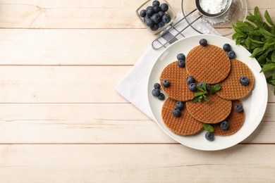 Photo of Tasty Dutch waffles (stroopwafels), mint and blueberries on light wooden table, flat lay. Space for text