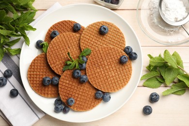 Photo of Tasty Dutch waffles (stroopwafels), mint and blueberries on light wooden table, flat lay