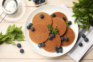 Photo of Tasty Dutch waffles (stroopwafels), mint and blueberries on light wooden table, flat lay