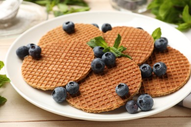 Photo of Tasty Dutch waffles (stroopwafels), mint and blueberries on light wooden table, closeup