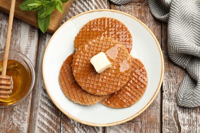 Photo of Tasty Dutch waffles (stroopwafels) with honey and butter cube on wooden table, flat lay