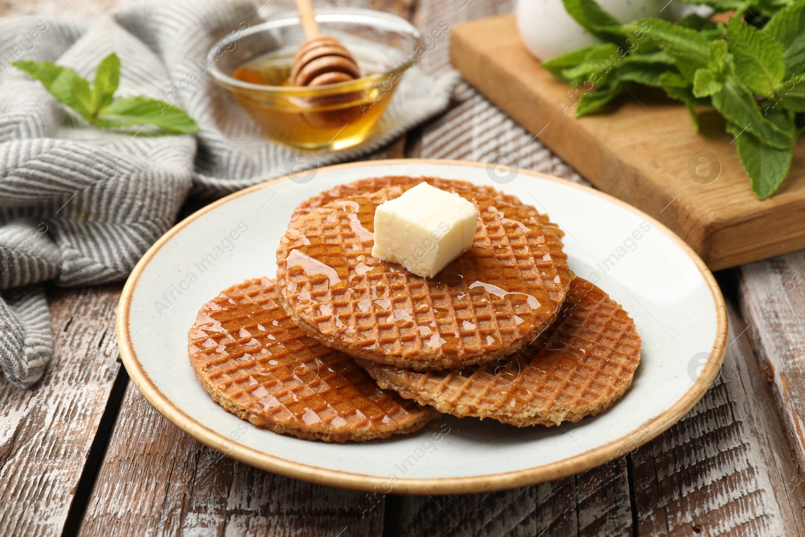 Tasty Dutch waffles (stroopwafels) with honey and butter cube on wooden table, closeup Photo of Tasty Dutch waffles (stroopwafels) with honey and butter cube on wooden table, closeup