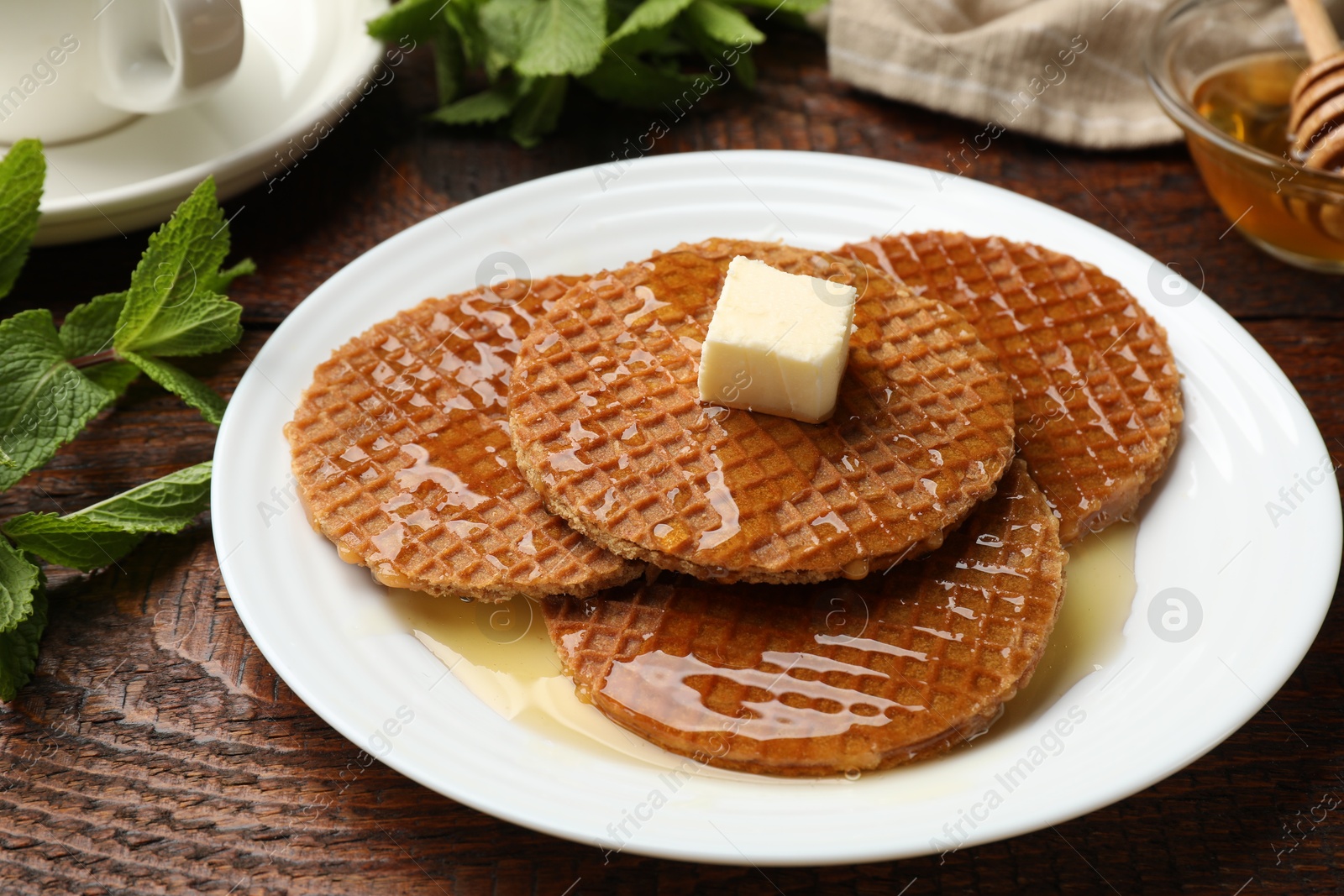 Tasty Dutch waffles (stroopwafels) with honey and butter cube on wooden table, closeup Photo of Tasty Dutch waffles (stroopwafels) with honey and butter cube on wooden table, closeup