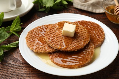 Photo of Tasty Dutch waffles (stroopwafels) with honey and butter cube on wooden table, closeup