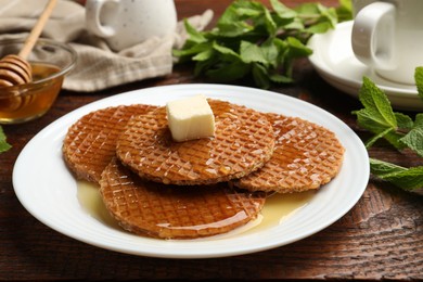 Photo of Tasty Dutch waffles (stroopwafels) with honey and butter cube on wooden table, closeup