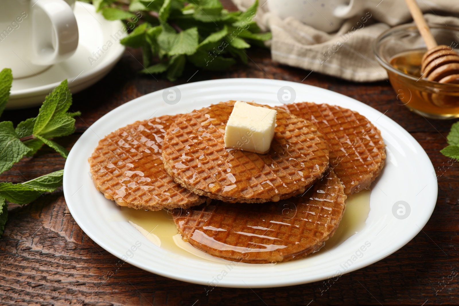 Tasty Dutch waffles (stroopwafels) with honey and butter cube on wooden table, closeup Photo of Tasty Dutch waffles (stroopwafels) with honey and butter cube on wooden table, closeup