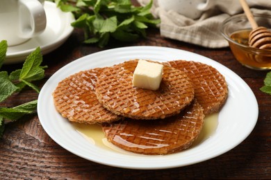 Photo of Tasty Dutch waffles (stroopwafels) with honey and butter cube on wooden table, closeup