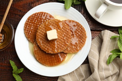 Photo of Tasty Dutch waffles (stroopwafels) with honey, butter cube and mint on wooden table, flat lay
