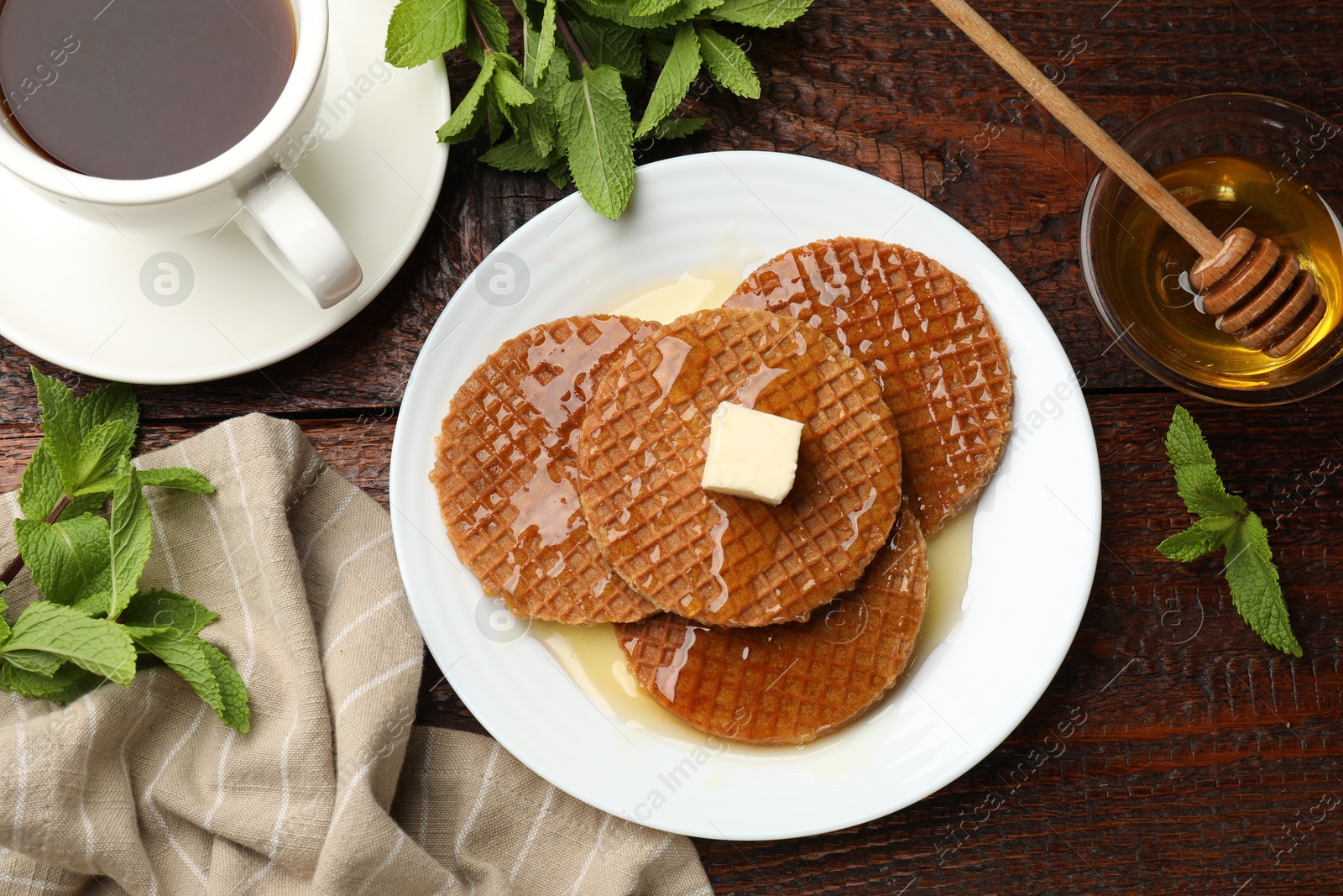 Tasty Dutch waffles (stroopwafels) with honey, butter cube, mint and tea on wooden table, flat lay Photo of Tasty Dutch waffles (stroopwafels) with honey, butter cube, mint and tea on wooden table, flat lay