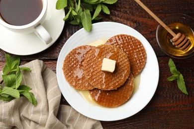 Photo of Tasty Dutch waffles (stroopwafels) with honey, butter cube, mint and tea on wooden table, flat lay
