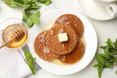 Photo of Tasty Dutch waffles (stroopwafels) with honey, butter cube and mint on white table, flat lay