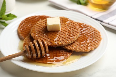 Photo of Tasty Dutch waffles (stroopwafels) with honey, butter cube and dipper on white marble table, closeup