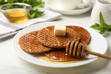 Photo of Tasty Dutch waffles (stroopwafels) with honey, butter cube and dipper on white marble table, closeup
