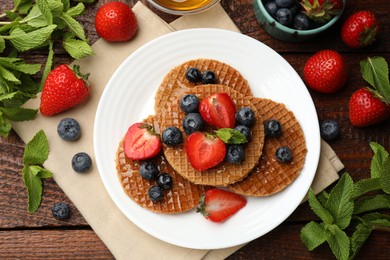 Photo of Tasty Dutch waffles (stroopwafels) with honey, berries and mint on wooden table, flat lay