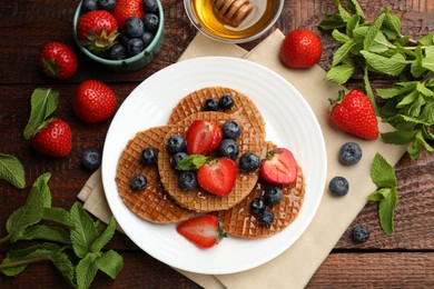 Photo of Tasty Dutch waffles (stroopwafels) with honey, berries and mint on wooden table, flat lay