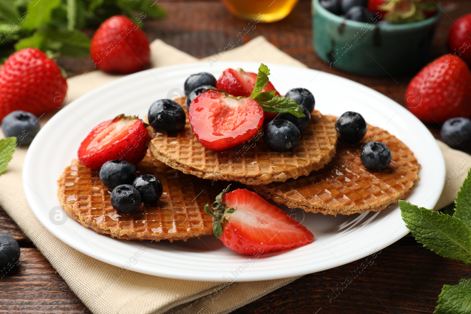 Tasty Dutch waffles (stroopwafels) with honey, berries and mint on wooden table, closeup Photo of Tasty Dutch waffles (stroopwafels) with honey, berries and mint on wooden table, closeup