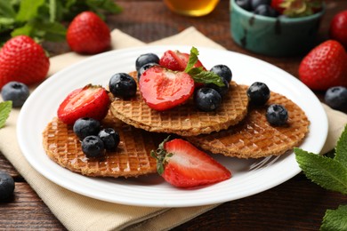 Photo of Tasty Dutch waffles (stroopwafels) with honey, berries and mint on wooden table, closeup