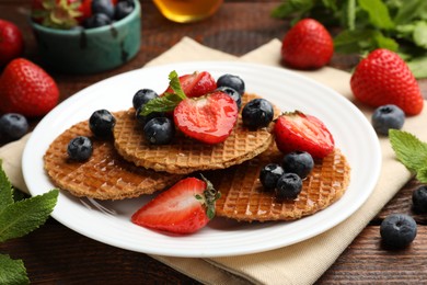 Photo of Tasty Dutch waffles (stroopwafels) with honey, berries and mint on wooden table, closeup