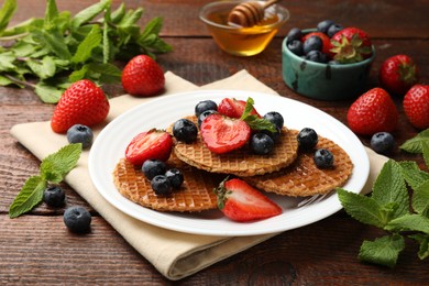 Photo of Tasty Dutch waffles (stroopwafels) with honey, berries and mint on wooden table, closeup