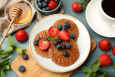 Photo of Tasty Dutch waffles (stroopwafels) with honey, berries and mint on light blue wooden table, flat lay