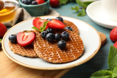 Photo of Tasty Dutch waffles (stroopwafels) with honey, berries and mint on light blue wooden table, closeup