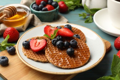 Photo of Tasty Dutch waffles (stroopwafels) with honey, berries and mint on light blue wooden table, closeup