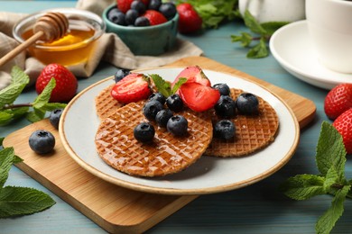 Photo of Tasty Dutch waffles (stroopwafels) with honey, berries and mint on light blue wooden table, closeup