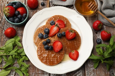 Photo of Tasty Dutch waffles (stroopwafels) with honey, berries and mint on wooden table, flat lay