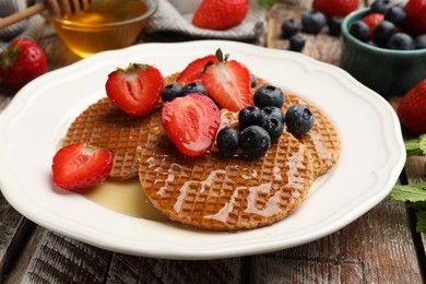 Photo of Tasty Dutch waffles (stroopwafels) with honey, strawberries and blueberries on wooden table, closeup