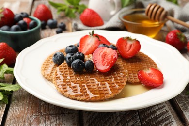Photo of Tasty Dutch waffles (stroopwafels) with honey, strawberries and blueberries on wooden table, closeup